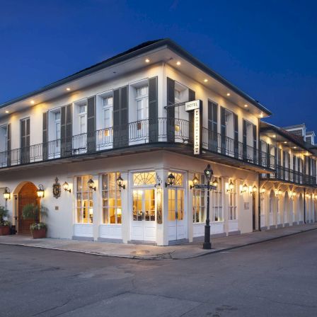 A two-story, white-painted corner building with large windows and string lights along the roofline at dusk, giving a quaint, inviting storefront vibe.