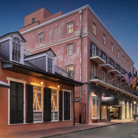 Colorful seaside street with pastel storefronts, balconies, and flags against a dusky sky.