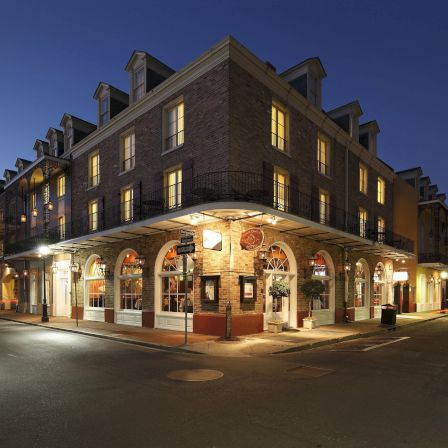A corner brick building at dusk with arched veranda, warm lights, and shops on the ground floor, forming a cozy downtown corner.