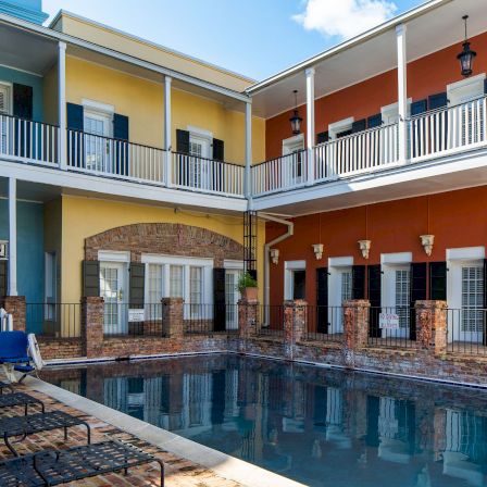Colorful motel courtyard with a rectangular pool, blue chairs, and pastel-covered two-story rooms surrounding the water.