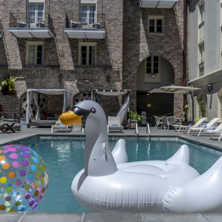 A floating white swan raft in a pool with colorful bubble balls and a brick hotel backdrop, sunny outdoor pool scene.