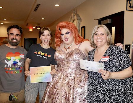 A group poses indoors at a Mardi Gras event—one person in a glittering corseted costume with red wig holds event tickets.