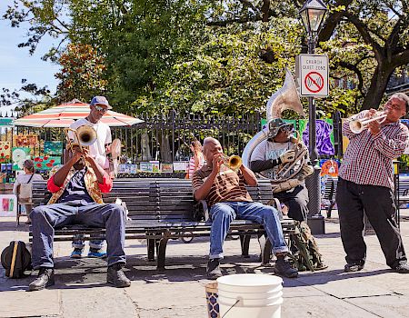 Street musicians play brass instruments on a park bench near a “CHURCH QUIET ZONE” sign, entertaining passersby with lively tunes.