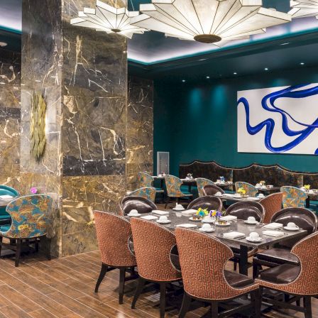 A stylish restaurant dining room with marble walls, blue graffiti art, chandelier lights, and set tables for guests.