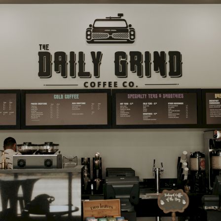 A coffee shop menu wall reads &ldquo;The Daily Grind Coffee Co.&rdquo; with hot drinks, cold coffee, teas, smoothies, and breakfast items on boards.