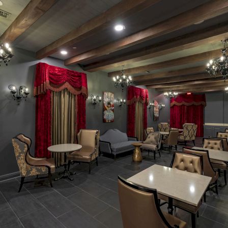 A stylish, dimly lit lounge with chandeliers, red drapes, comfy seating, and small tables for intimate conversations.