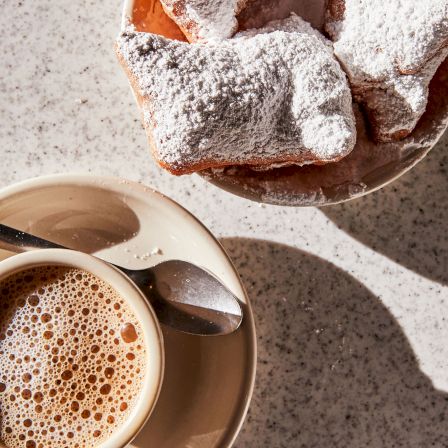 Powdered-sugar pastries and toast pieces sit by a cup of coffee on a speckled plate.