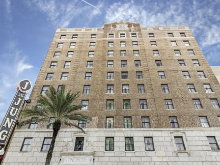 A tall brick hotel building with rows of windows under a blue sky, palm tree in front and a street sign at left.