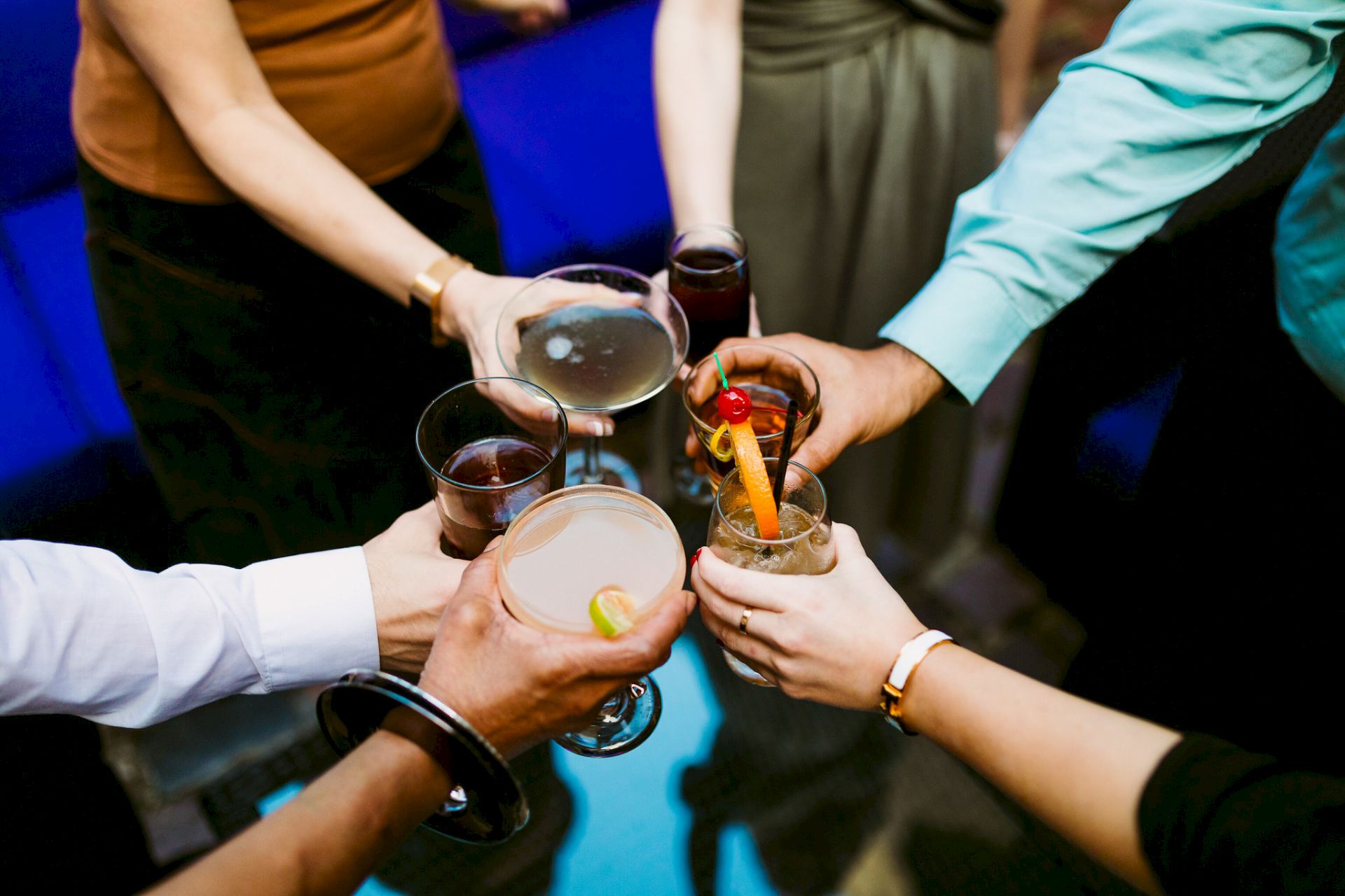 Friends clink glasses of cocktails with garnished drinks in a lively toast at a gathering.